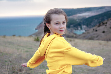 Preteen girl traveler wearing yellow hoodie walking  on top of the mountain landscape and looking to the sea