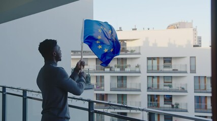 Young black man asylum seeker waving european union flag from the balcony. High quality 4k footage
