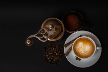 Aged coffee grinder, cup of coffee on saucer, coffee beans, anise, cinnamon sticks, ground coffee