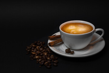 White cup of hot coffee, cinnamon sticks, coffee beans on black background