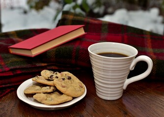 Fresh homemade warm comforting chocolate chip cookies ready to eat and enjoy with cozy mug of tea and relaxing with a book on a cold winter afternoon
