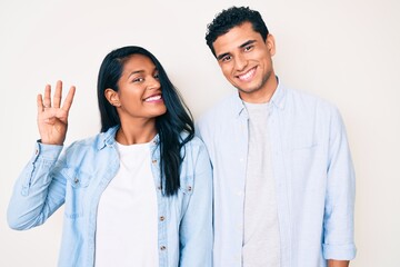 Fototapeta na wymiar Beautiful latin young couple wearing casual clothes showing and pointing up with fingers number four while smiling confident and happy.