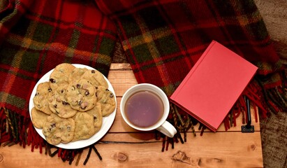 Fresh homemade warm comforting chocolate chip cookies ready to eat and enjoy with cozy mug of tea and relaxing with a book on a cold winter afternoon
