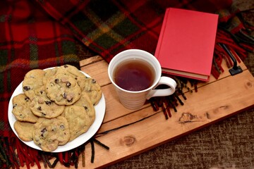 Fresh homemade warm comforting chocolate chip cookies ready to eat and enjoy with cozy mug of tea and relaxing with a book on a cold winter afternoon