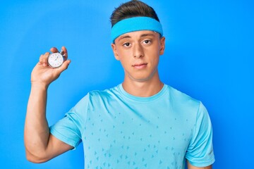 Young hispanic boy holding stopwatch thinking attitude and sober expression looking self confident