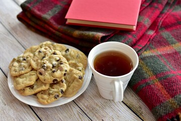 Fresh homemade warm comforting chocolate chip cookies ready to eat and enjoy with cozy mug of tea and relaxing with a book on a cold winter afternoon