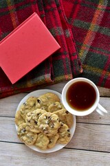 Fresh homemade warm comforting chocolate chip cookies ready to eat and enjoy with cozy mug of tea and relaxing with a book on a cold winter afternoon