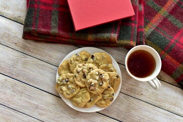 Fresh homemade warm comforting chocolate chip cookies ready to eat and enjoy with cozy mug of tea and relaxing with a book on a cold winter afternoon