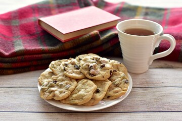 Fresh homemade warm comforting chocolate chip cookies ready to eat and enjoy with cozy mug of tea and relaxing with a book on a cold winter afternoon