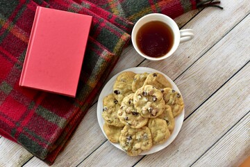 Fresh homemade warm comforting chocolate chip cookies ready to eat and enjoy with cozy mug of tea and relaxing with a book on a cold winter afternoon