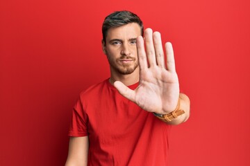 Handsome caucasian man wearing casual red tshirt doing stop sing with palm of the hand. warning expression with negative and serious gesture on the face.