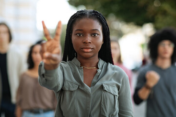Black woman leading group of international protestors, showing peace gesture