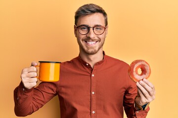 Fototapeta premium Handsome caucasian man eating doughnut and drinking coffee smiling with a happy and cool smile on face. showing teeth.