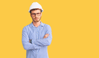 Handsome young man with bear wearing architect hardhat skeptic and nervous, disapproving expression on face with crossed arms. negative person.