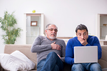 Father and son sitting on the sofa with computer