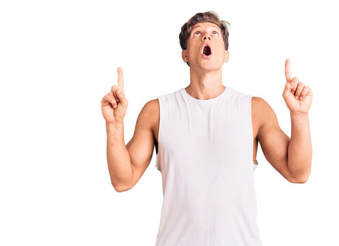 Young handsome man wearing sleveeless t shirt amazed and surprised looking up and pointing with fingers and raised arms.