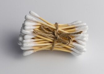 Eco-friendly wooden cotton ear sticks or ear swabs made without plastic connected with roap with white background. Sustainability and recycling worldwide problems.