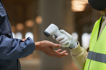 Side view close up of supervisor measuring temperature of workers with contactless thermometer pointing at hands, copy space