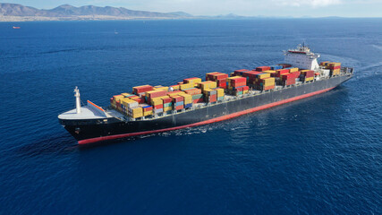 Aerial drone photo of huge container tanker ship carrying truck size colourful containers in deep blue open ocean sea