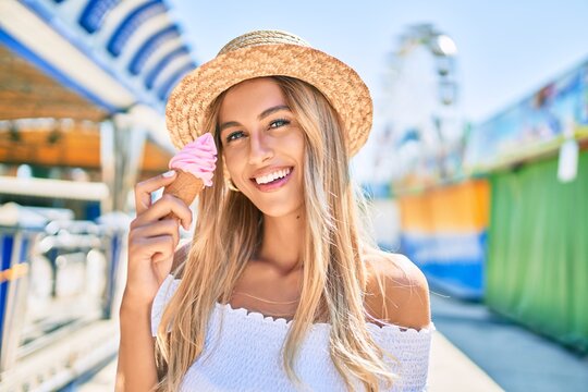 Young blonde tourist girl smiling happy eating ice cream at the fairground.