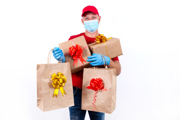 Safe contactless remote delivery of holiday gifts during coronavirus pandemic. A courier in red uniform and protective medical mask and gloves holds large order, many gift boxes and bags with bows