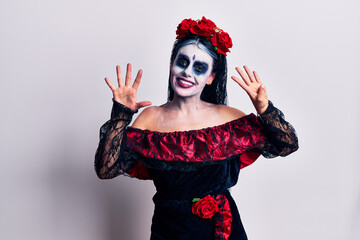 Young woman wearing mexican day of the dead makeup showing and pointing up with fingers number nine while smiling confident and happy.