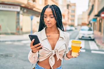 Young african american woman with serious expression using smartphone and drinking coffee at the city.