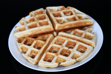 Belgian waffles in white plate on black glass table. Healthy breakfast, pieces of freshly baked classic wafer