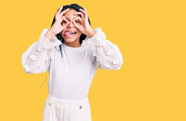 Cute african american girl wearing casual white tshirt doing ok gesture like binoculars sticking tongue out, eyes looking through fingers. crazy expression.