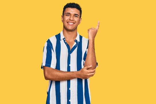 Young arab man wearing casual clothes with a big smile on face, pointing with hand and finger to the side looking at the camera.