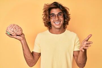 Young hispanic man holding brain celebrating achievement with happy smile and winner expression...