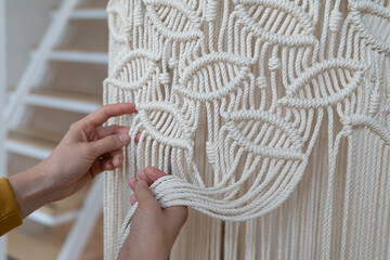 Freelancer woman working on half-finished macrame piece, weaves lamp shade for chandelier. Women hobby.