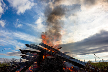 Naklejka premium View of a large campfire with black smoke rising into the blue sky 