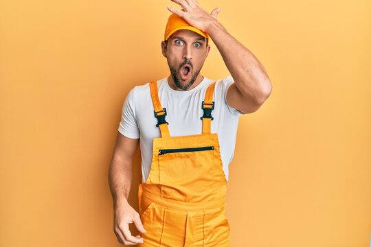 Young handsome man wearing handyman uniform over yellow background surprised with hand on head for mistake, remember error. forgot, bad memory concept.