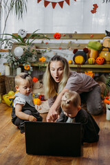 Fototapeta premium Halloween Holidays, Online Holiday party in the Time of COVID. Happy family, mother and baby celebrating Halloween near laptop, online meeting in new normal, Pandemic time.