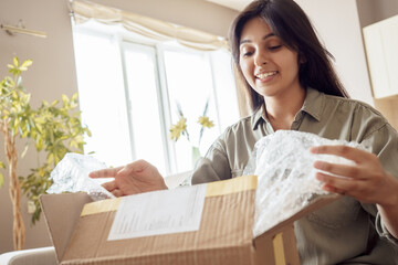 Smiling indian woman shopper customer opening post package box sitting on couch at home. Happy...