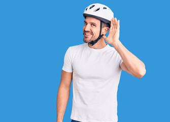 Young handsome man wearing bike helmet smiling with hand over ear listening an hearing to rumor or gossip. deafness concept.