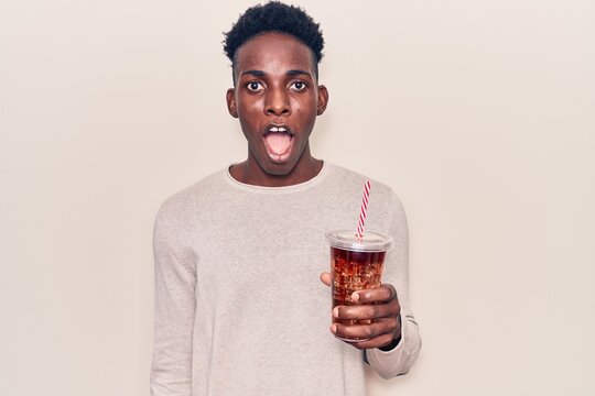 Young african american man drinking mate infusion scared and amazed with open mouth for surprise, disbelief face