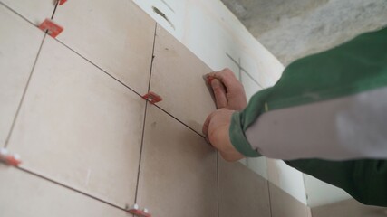The master puts the tiles in the bathrooms.. Master in overalls puts ceramic tiles on the wall