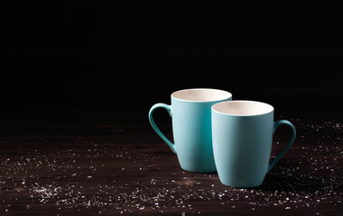 Two empty blue mugs stand against a dark wooden background with snow