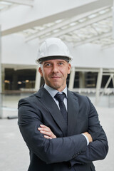 Vertical waist up portrait of smiling mature businessman wearing hardhat and looking at camera...