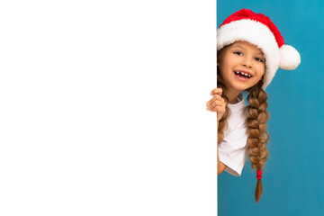 A little girl in a Christmas hat looks out from behind an ad.