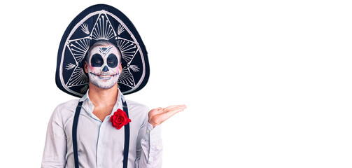 Man wearing day of the dead costume over background smiling cheerful presenting and pointing with palm of hand looking at the camera.