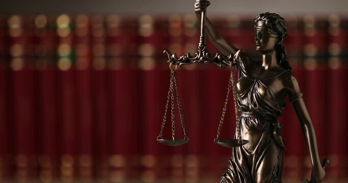 bronze blindfolded goddess representing law statue spinning, holding a scale and sword symbolizing impartiality and two broad sources of law in a university room with a background made of books