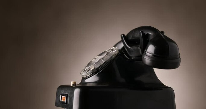 side view of black old rotary telephone slowly spinning and rotating on brown background 