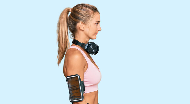 Young blonde woman wearing gym clothes and using headphones looking to side, relax profile pose with natural face with confident smile.