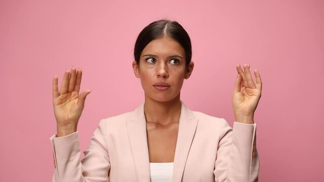 young businesswoman in pink suit rolling eyes, holding arms in the air and making a talking hands gesture on pink background