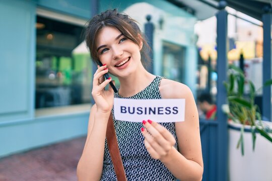Young caucasian businesswoman talking on the smartphone and holding business word paper at the city.