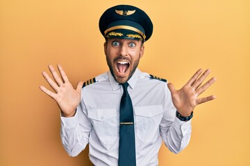 Handsome hispanic man wearing airplane pilot uniform celebrating crazy and amazed for success with arms raised and open eyes screaming excited. winner concept