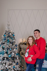 Happy family of three, young mother expecting a new baby, father and their little son near decorated Christmas tree